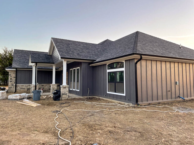 Newly built gray board-and-batten home with white porch columns