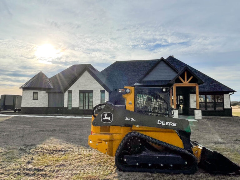 Skid steer grading the yard in front of a newly built custom home