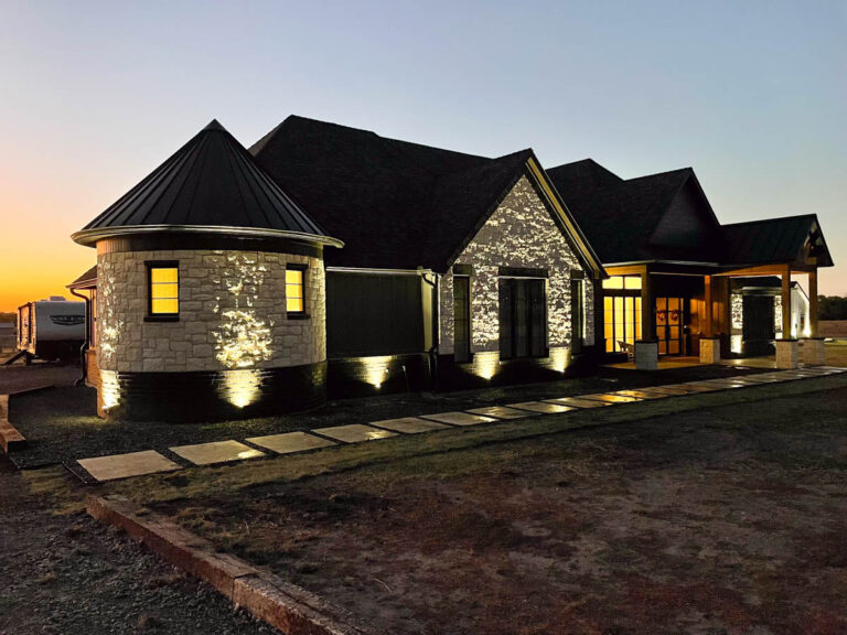 Stone custom home with a turret entry lit up at dusk