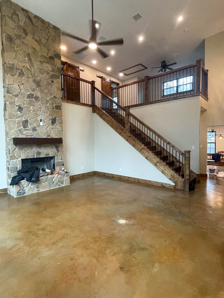 Living room with a stone fireplace, stained concrete floors and an open staircase