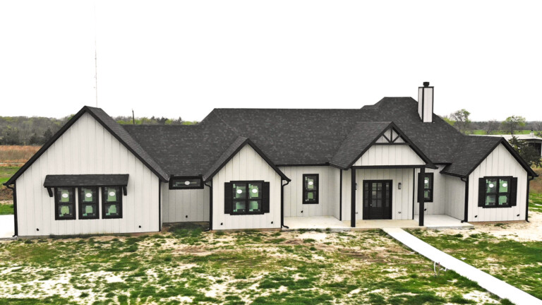 White custom home with a dark roof and black windows on a new lot