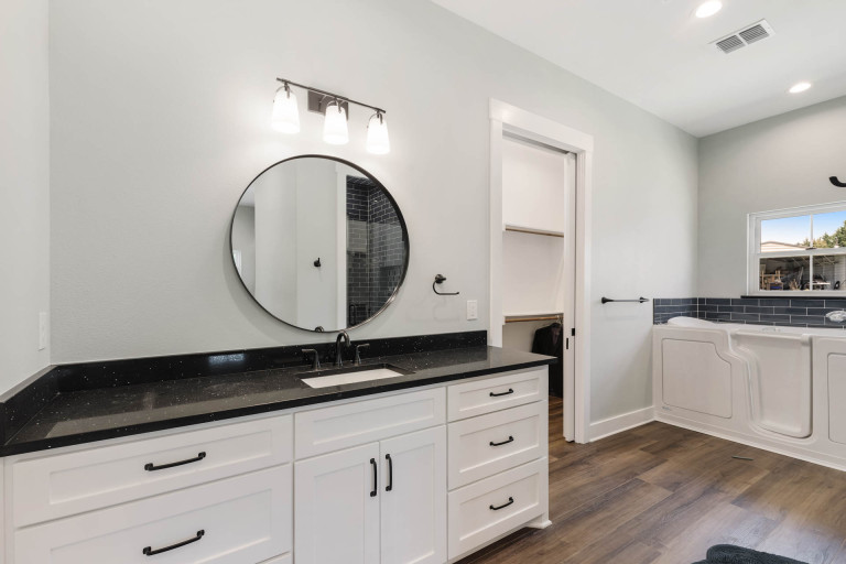 Bathroom vanity with white shaker cabinets, black countertop and round mirror
