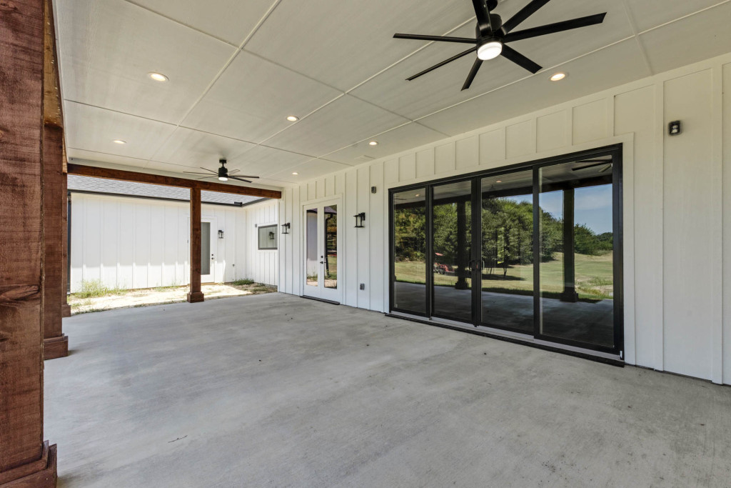 Large covered patio with black sliding doors, white board-and-batten walls and ceiling fan