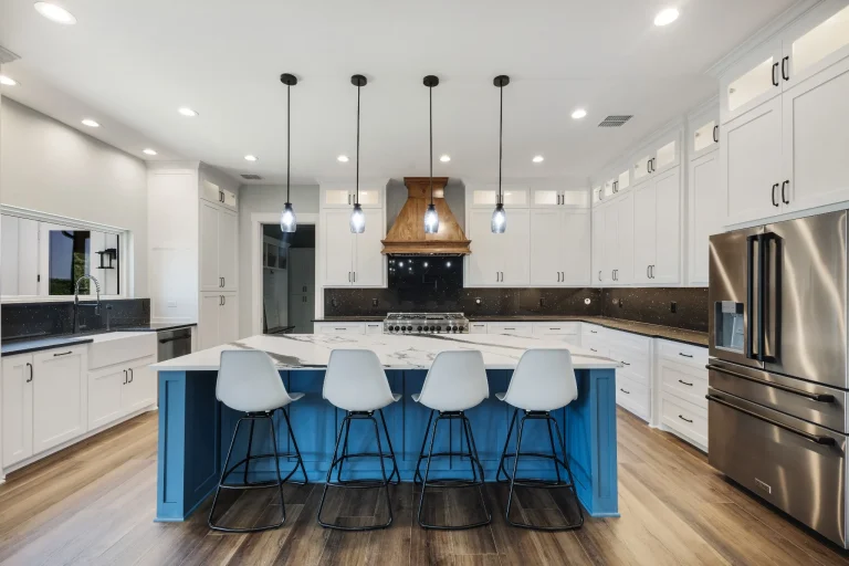 Blue kitchen island with white stools and stainless refrigerator
