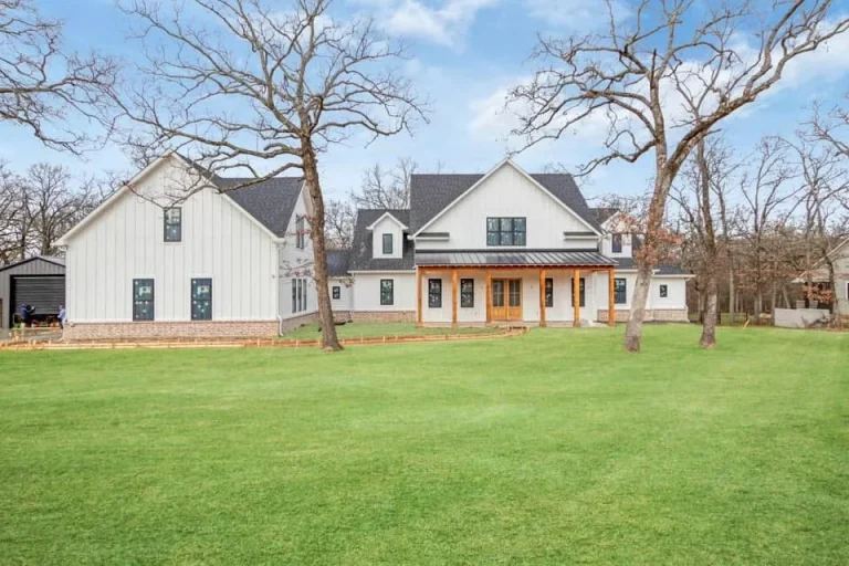 Side of the white board-and-batten farmhouse on a wooded lot