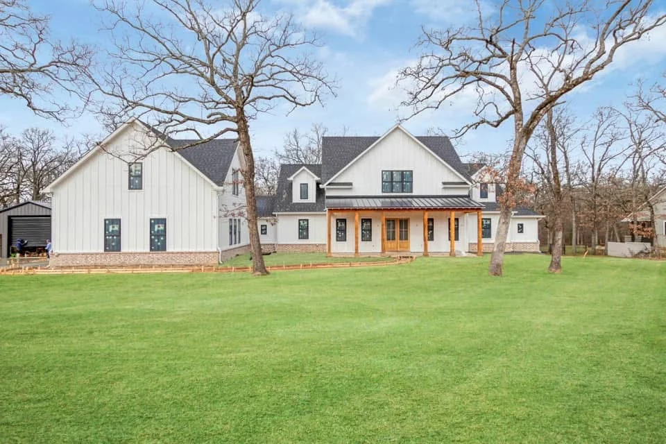 Side of the white board-and-batten farmhouse on a wooded lot